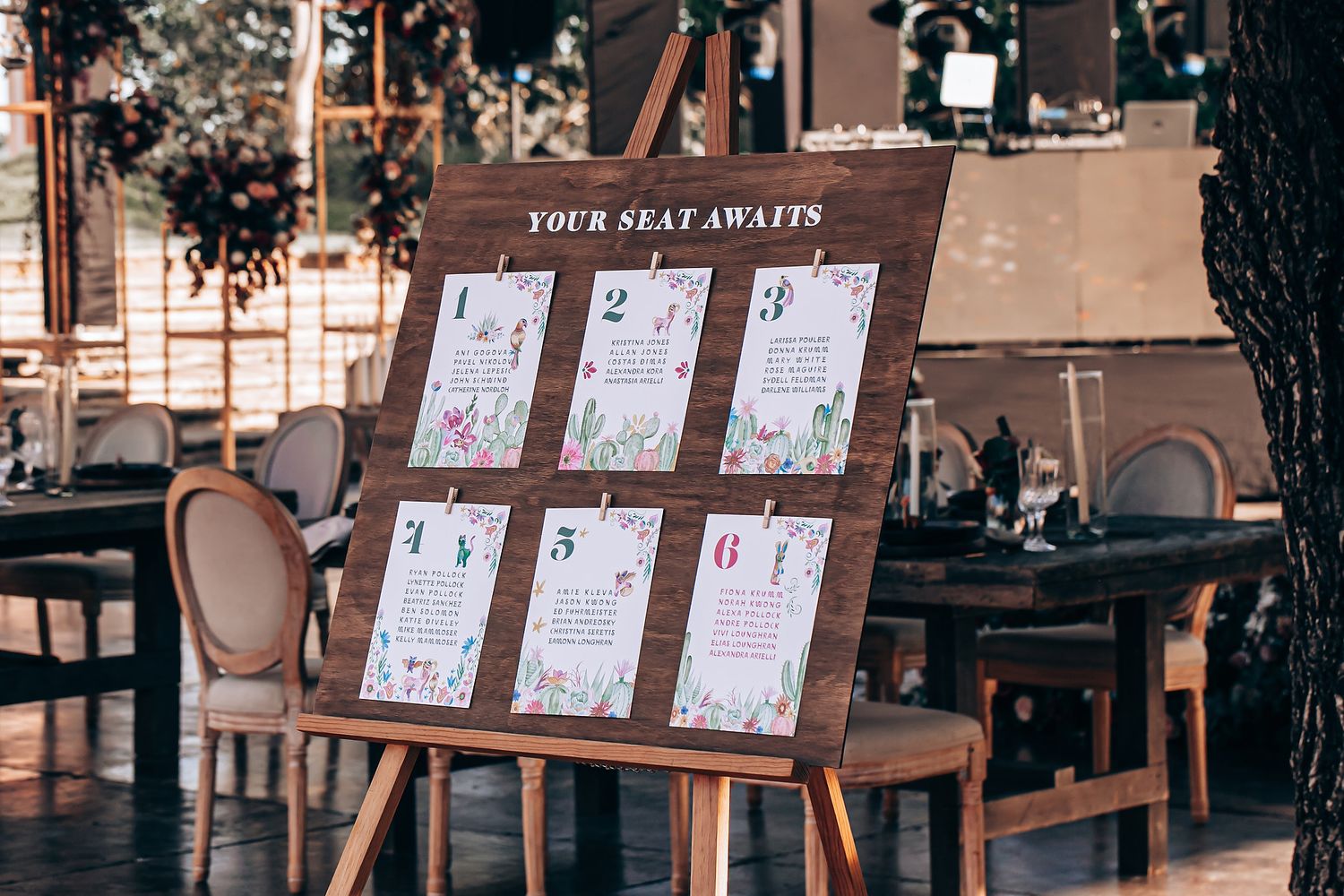 Wedding seating chart display with floral design cards mounted on wooden board at reception venue.