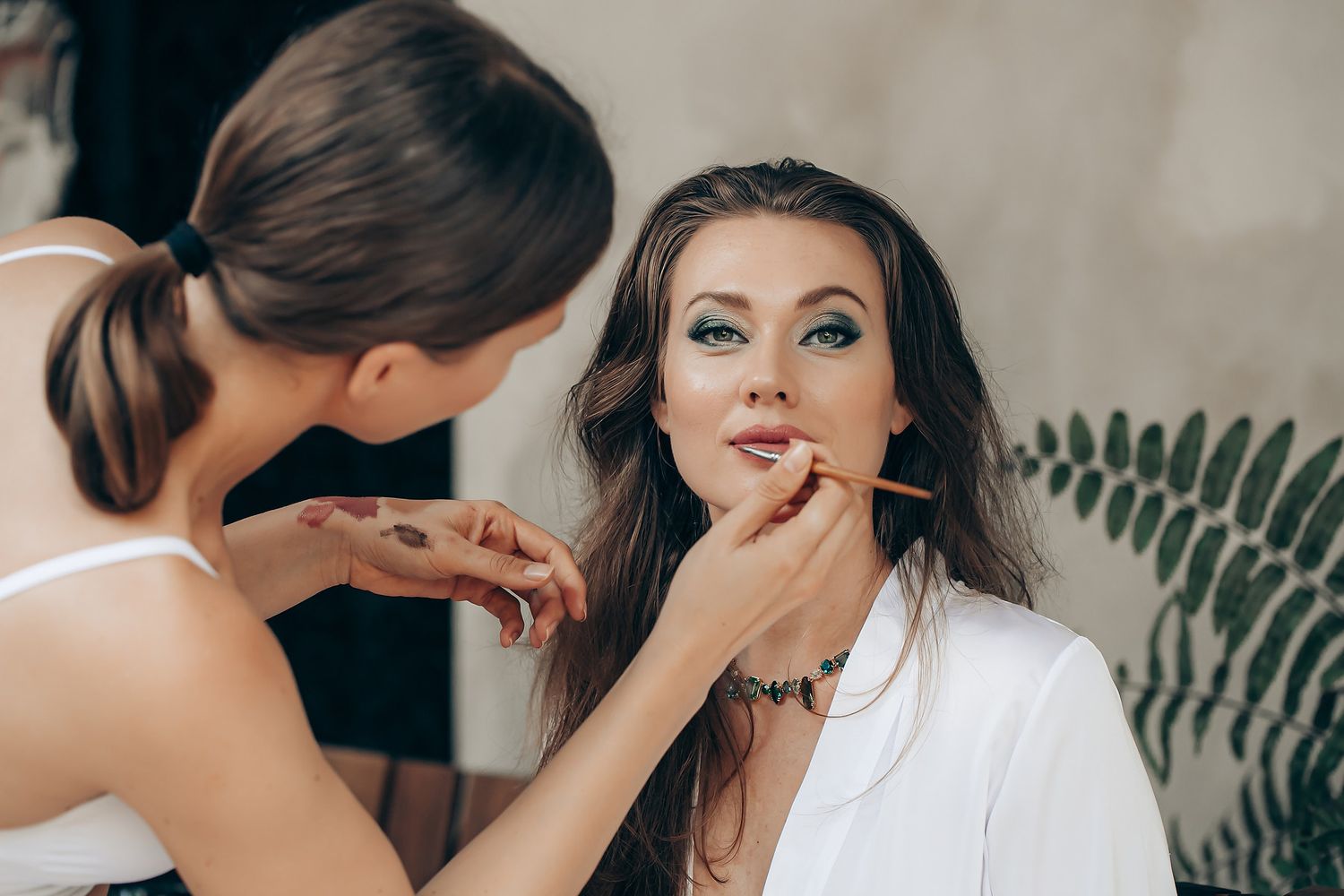 Professional makeup artist applying eyeshadow to client during beauty session with brushes and cosmetics.