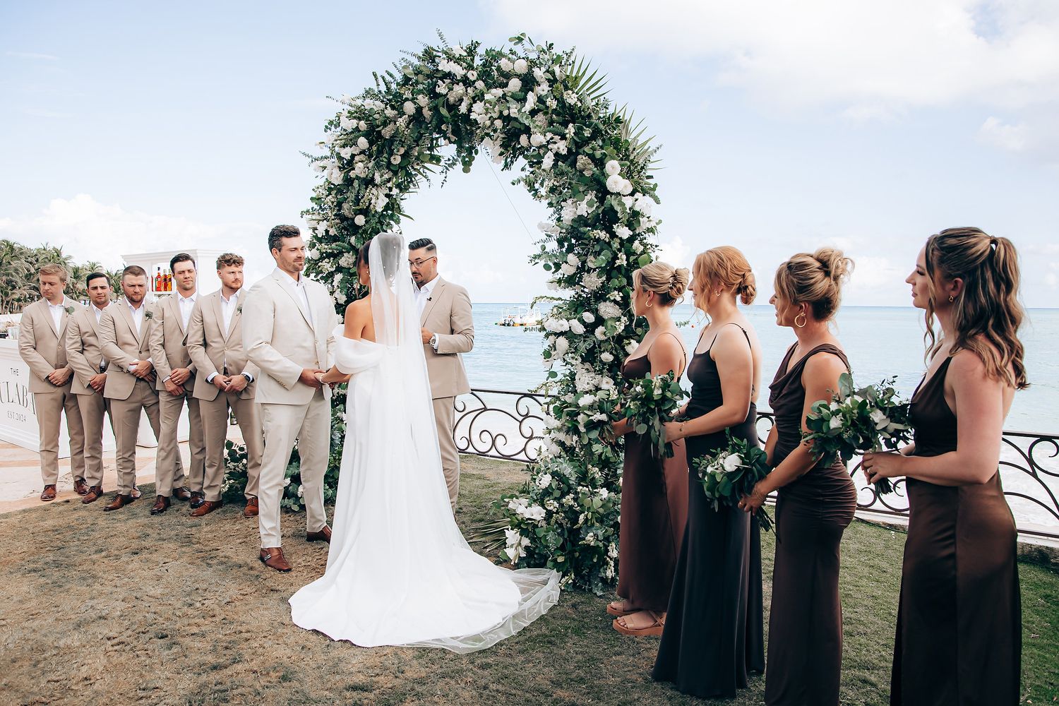 Wedding party in neutral tones gathered outdoors with bridesmaids in brown dresses.