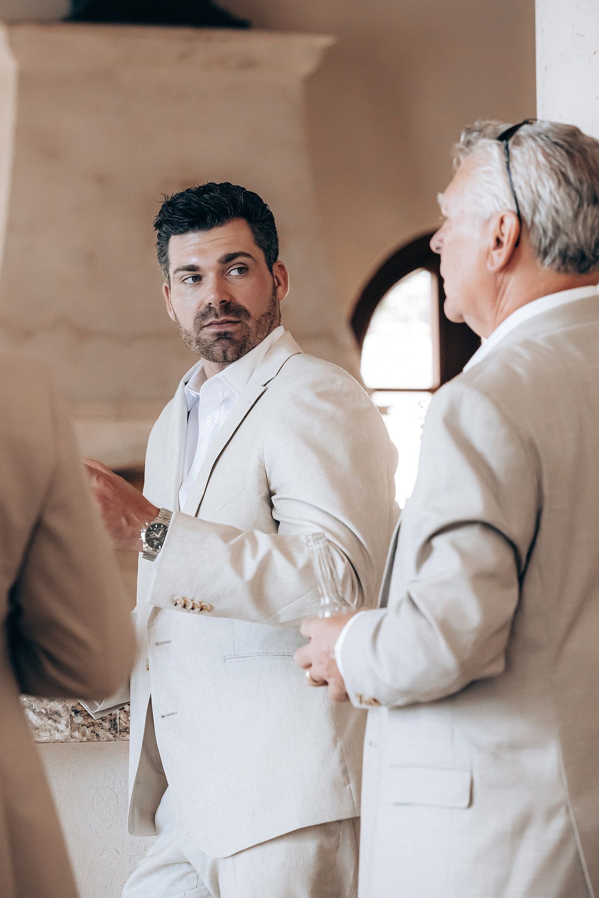 Groomsmen in cream-colored suits help each other get ready before a wedding ceremony.