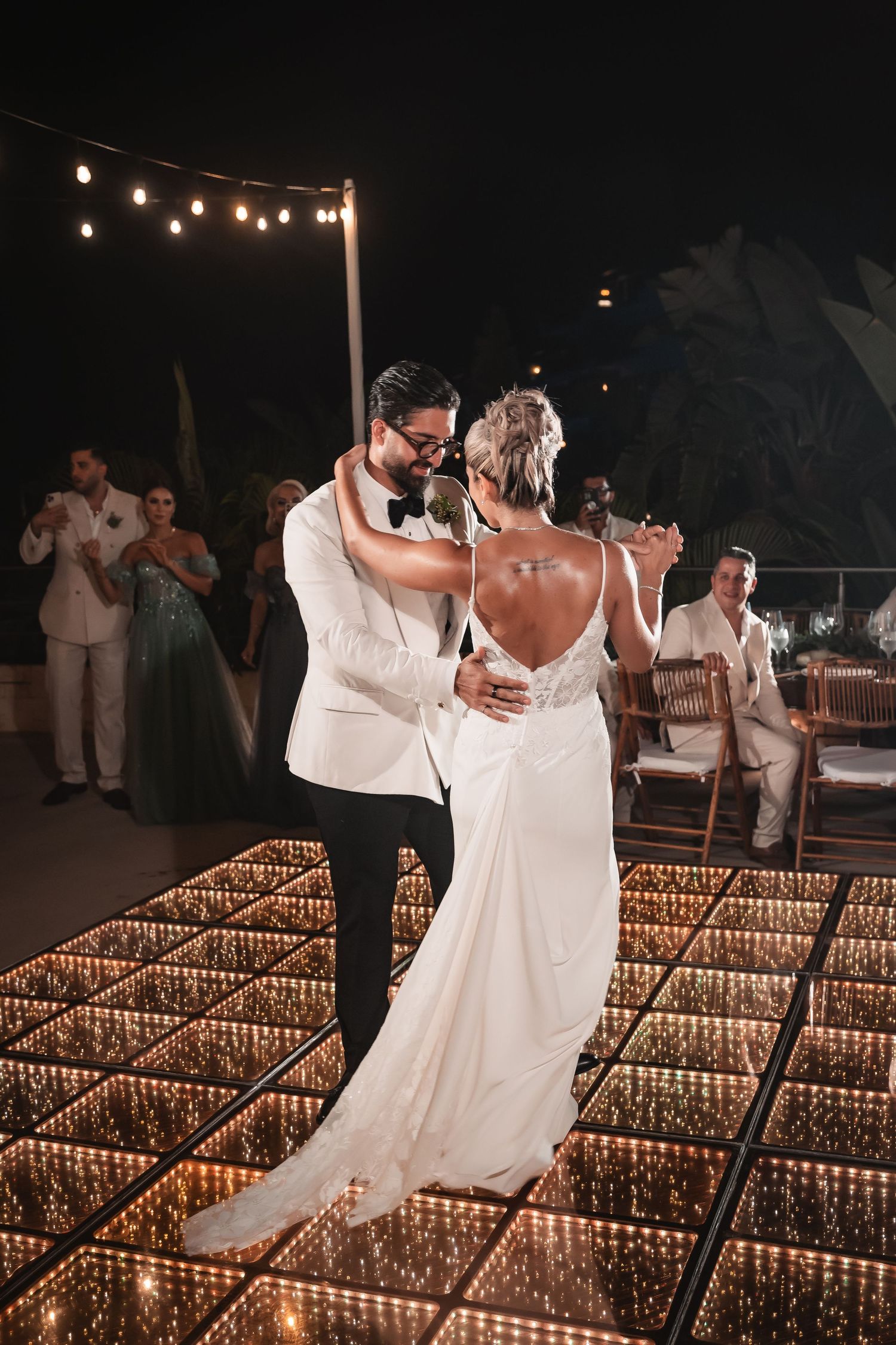 Couple dancing on an illuminated platform under string lights at their evening wedding reception.