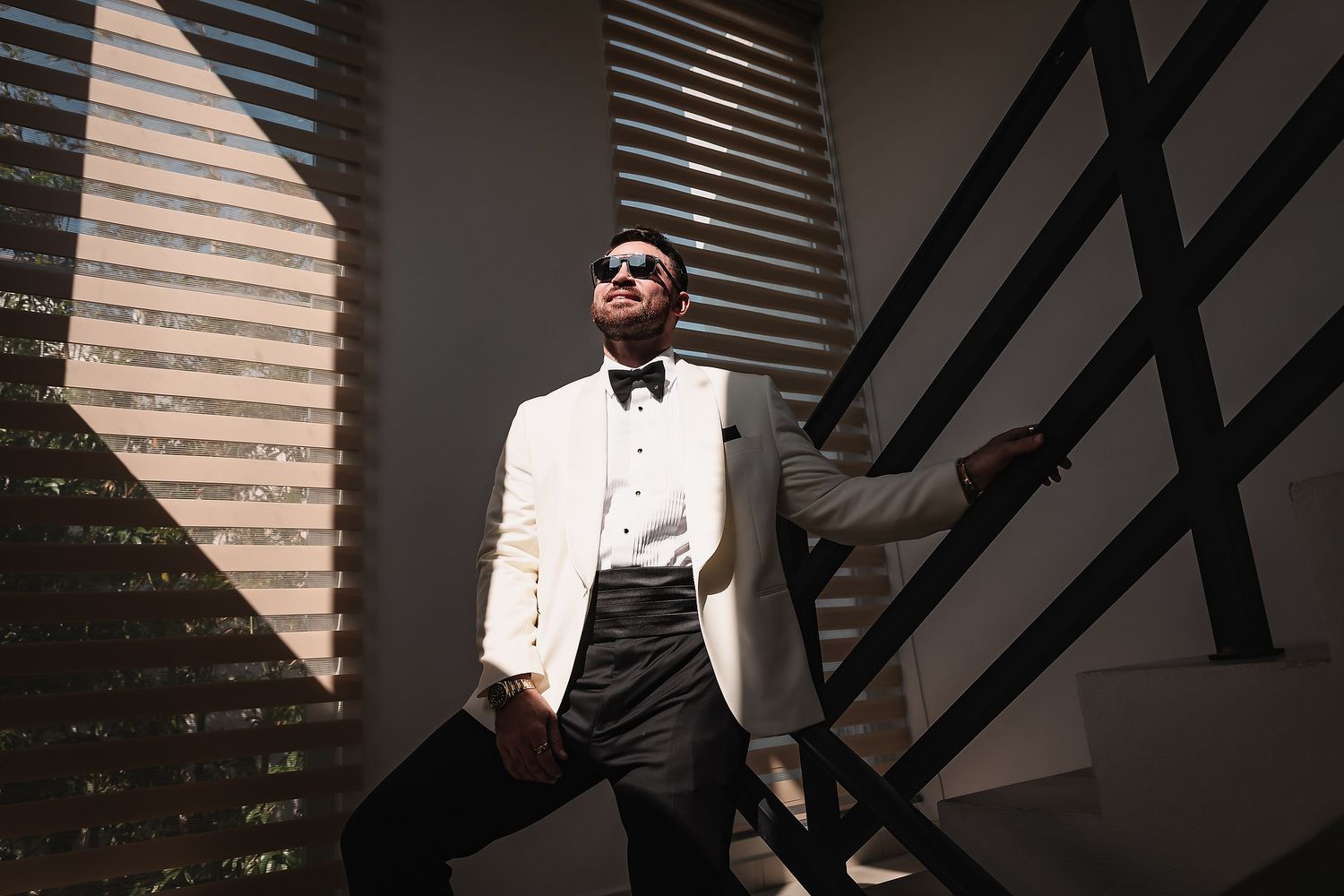 Dramatic black and white portrait with venetian blinds creating striking shadow patterns.