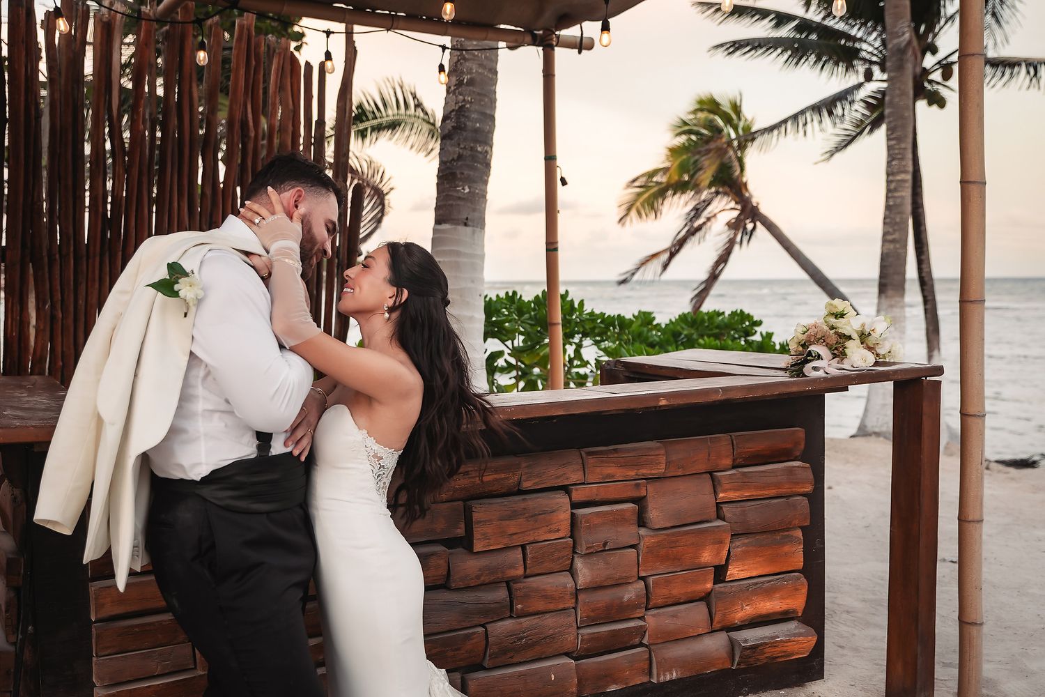 Romantic beachside wedding portraits with palm trees and wooden structures in the background.