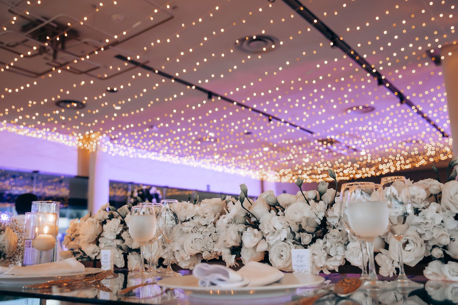An elegant wedding reception venue decorated with twinkling fairy lights and white floral arrangements.