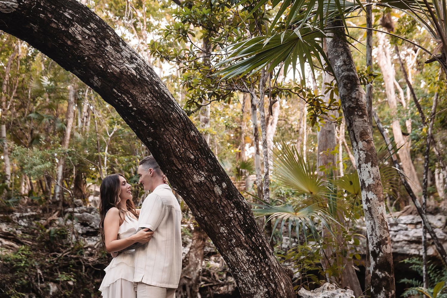 Couple's portrait session under arching tree branches in natural outdoor setting.