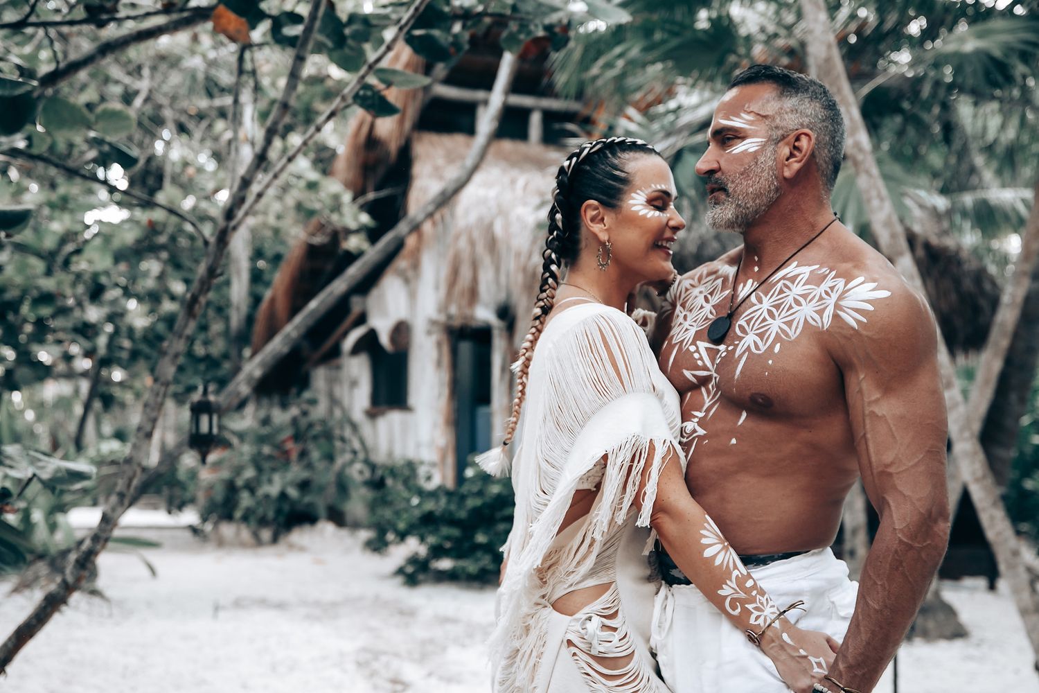 A couple in white beach attire poses against lush tropical foliage.