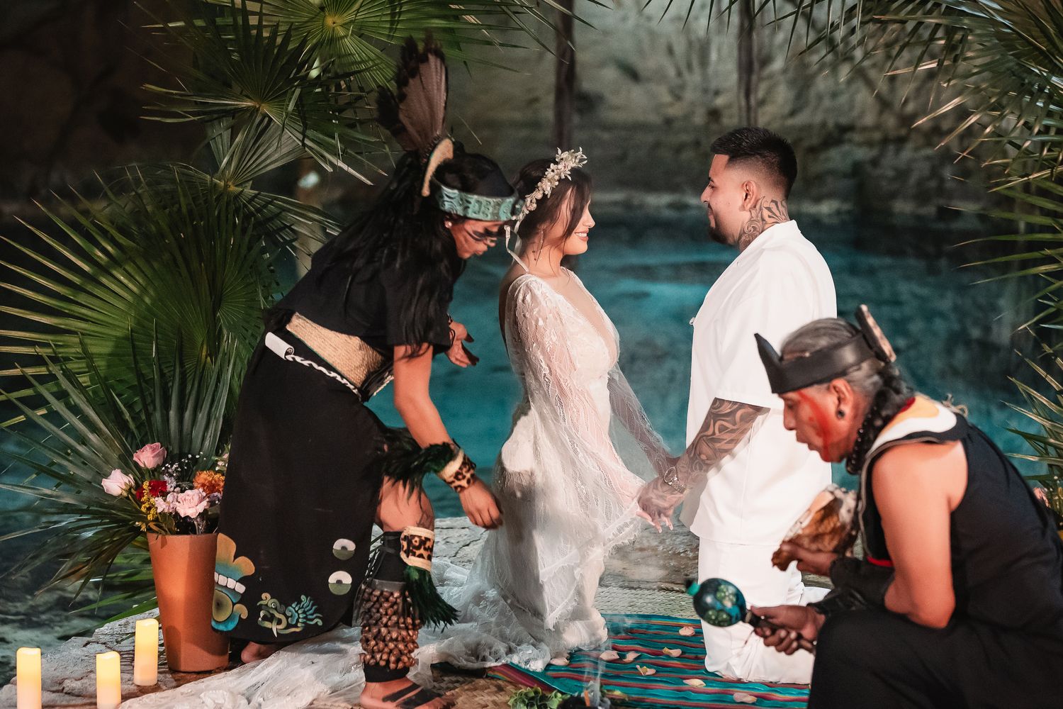 Intimate wedding ceremony setup in a cave with candles and tropical decorations beside turquoise waters.