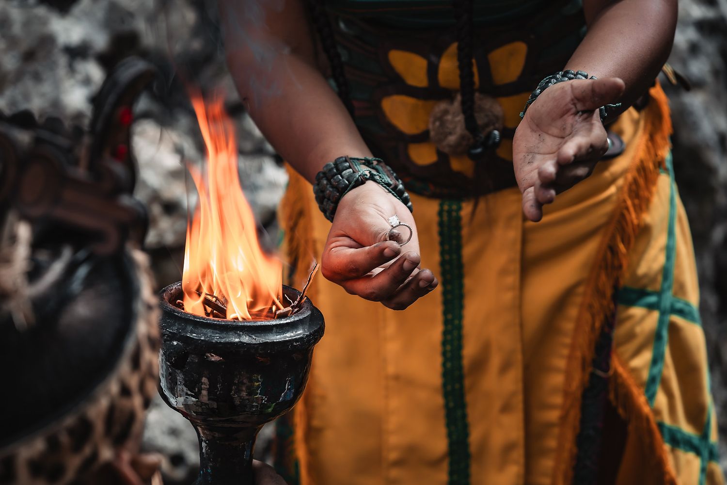 Close-up of ceremonial fire burning in a vessel with hands holding ritual objects.