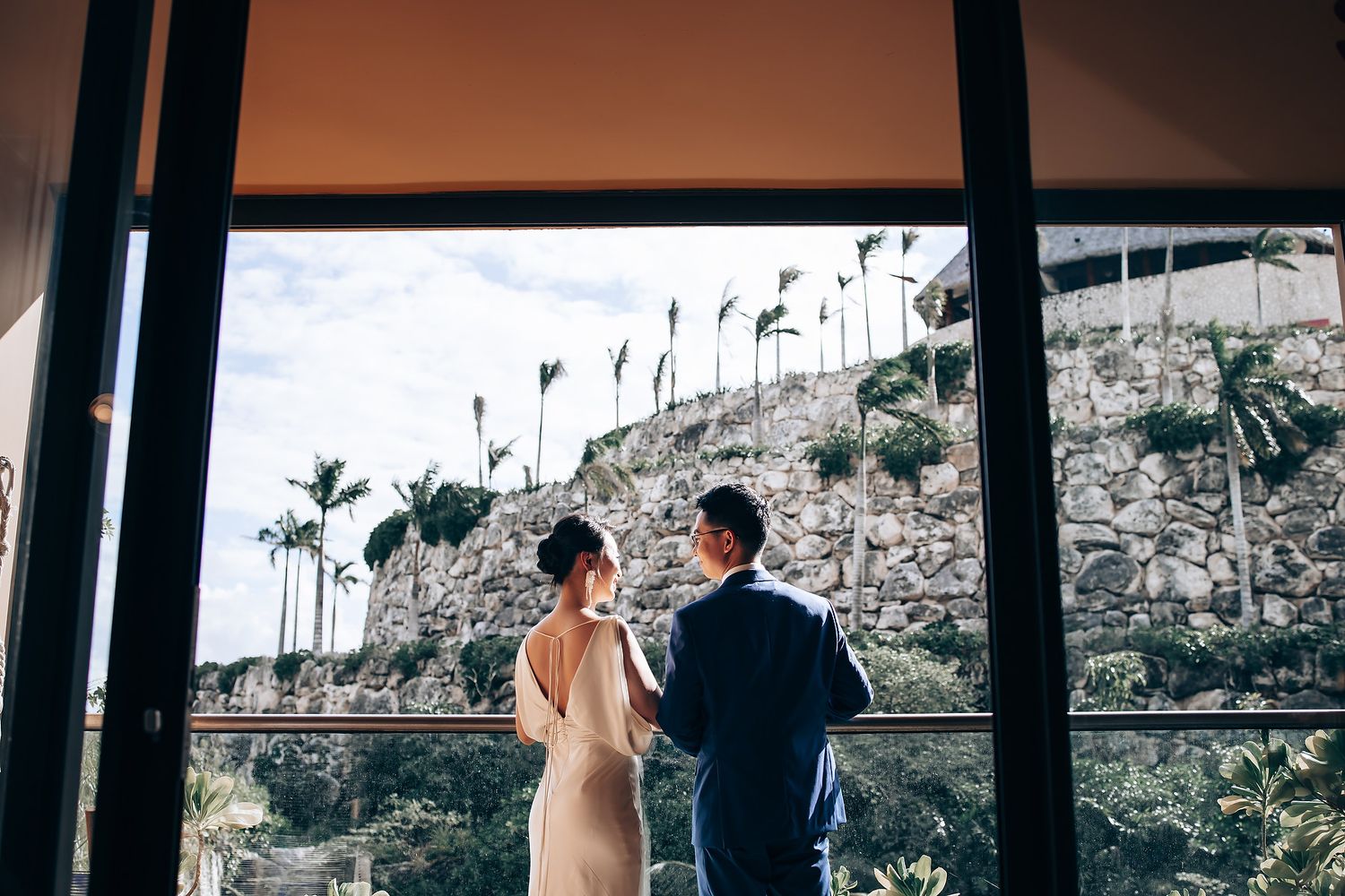 A wedding ceremony takes place at a beautiful outdoor venue with palm trees and mountains in the background.