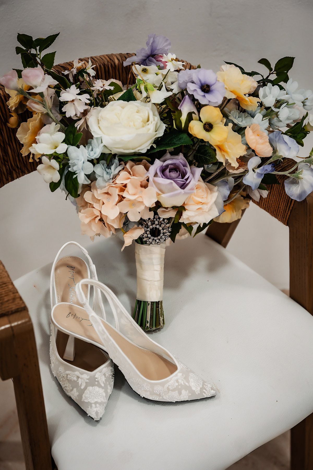 Bridal bouquet of colorful flowers with white lace heels on a wooden chair for a wedding.