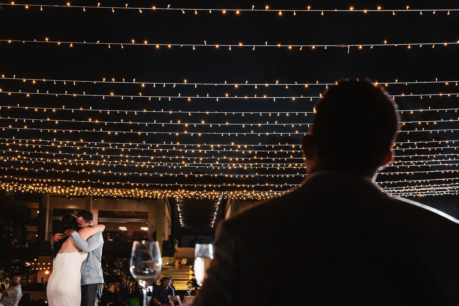 Couple shares first dance under romantic string lights at outdoor wedding reception at night.