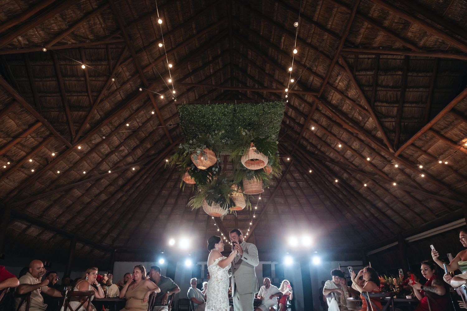 Couple celebrates first dance under string lights and lush greenery in a rustic barn wedding venue.