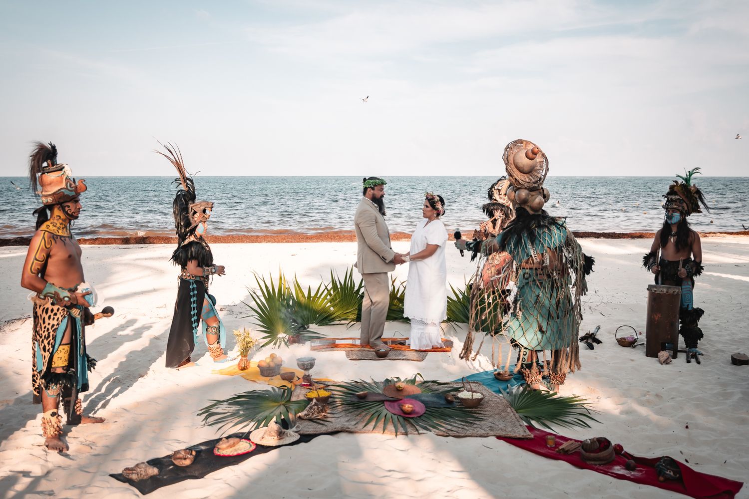 Mayan ceremony on a white sand beach with performers in traditional costumes celebrating a wedding by the ocean.