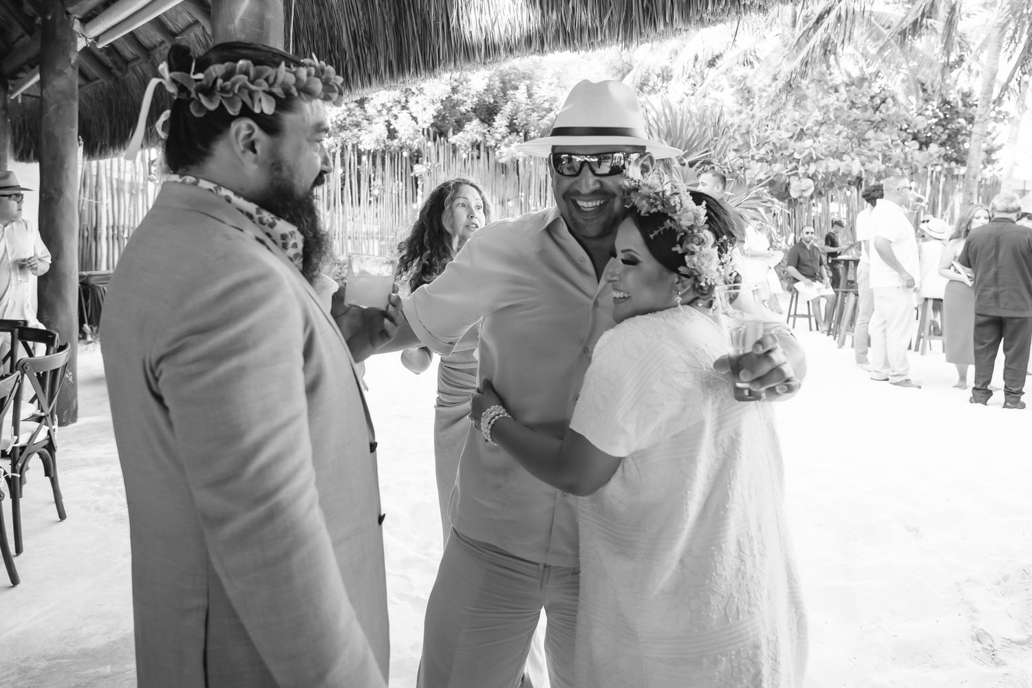 Black and white beach wedding photo of guests embracing and celebrating near a thatched palapa.