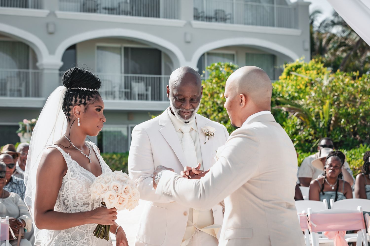 Bride and groom exchange vows with officiant at outdoor wedding ceremony near resort pool.