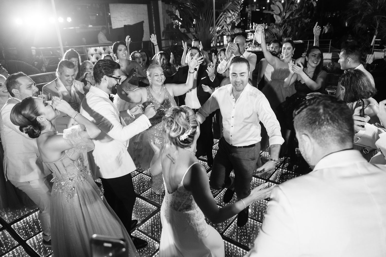 Energetic black and white photo of wedding guests dancing together at a lively reception party.
