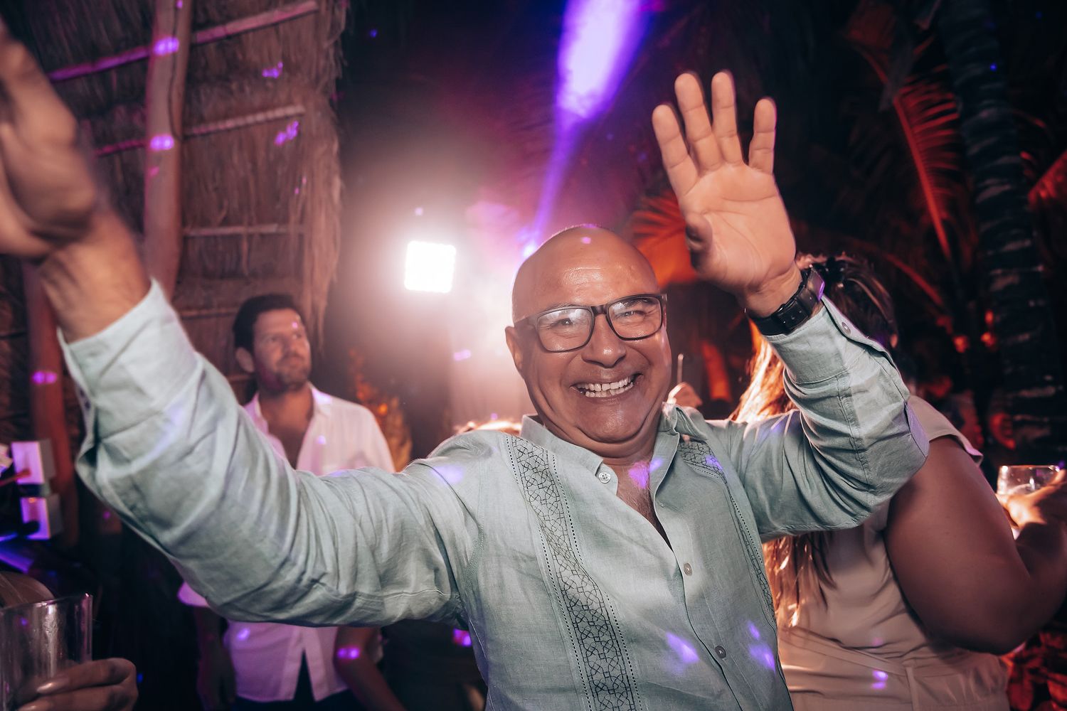 Party guests dancing and celebrating under colorful lighting at a nighttime event.