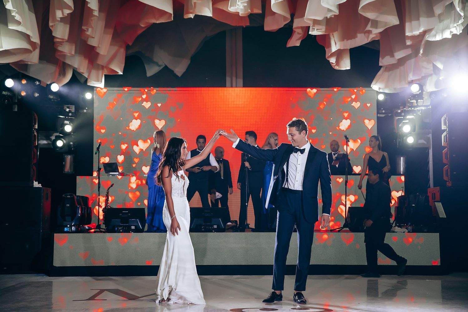 First dance in elegant ballroom with red lighting and dramatic shadows.
