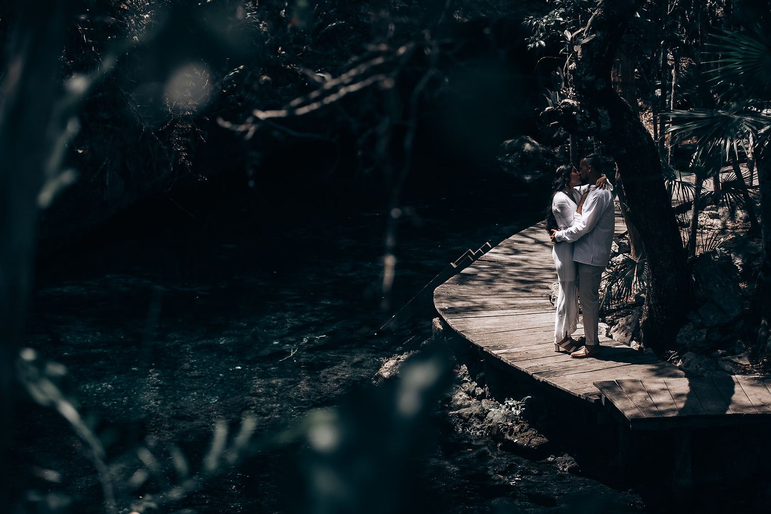 A silhouetted couple stands on a wooden platform surrounded by dark forest scenery.
