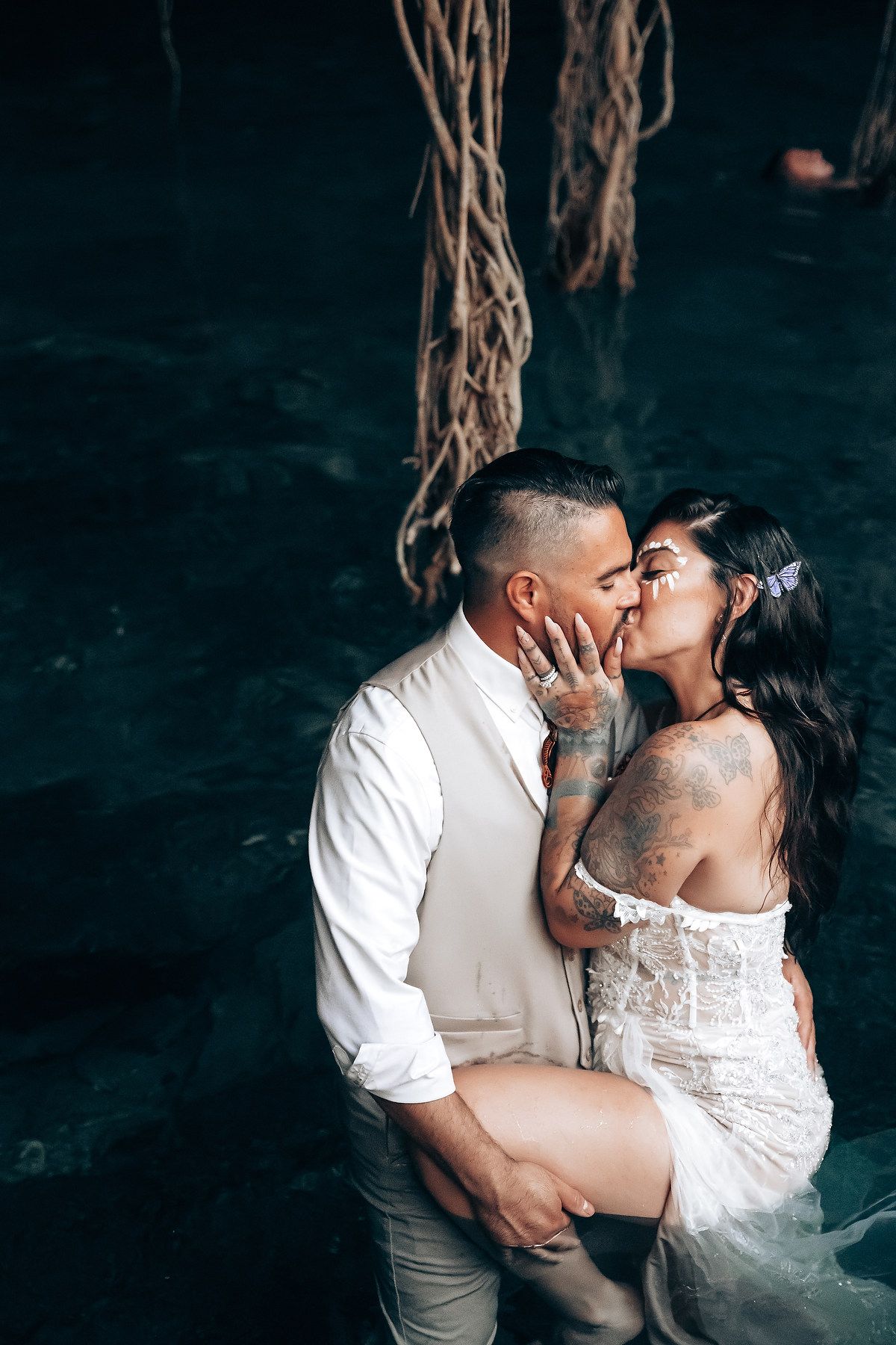 A romantic couple shares intimate kisses against a dark background in wedding attire.
