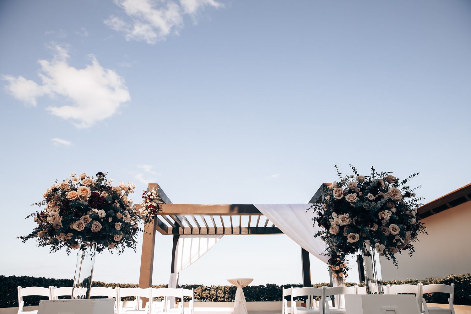 An outdoor wedding ceremony with floral arrangements and a wooden arch.