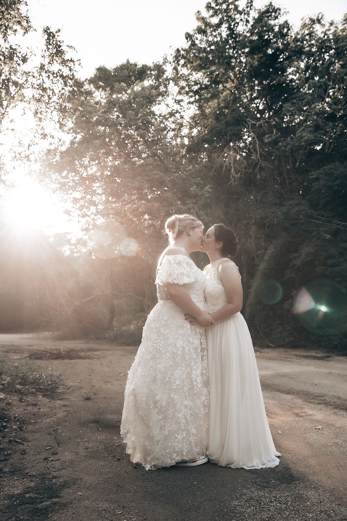 The image captures a bride and groom embracing in a sunlit, wooded area, creating a romantic and serene atmosphere.