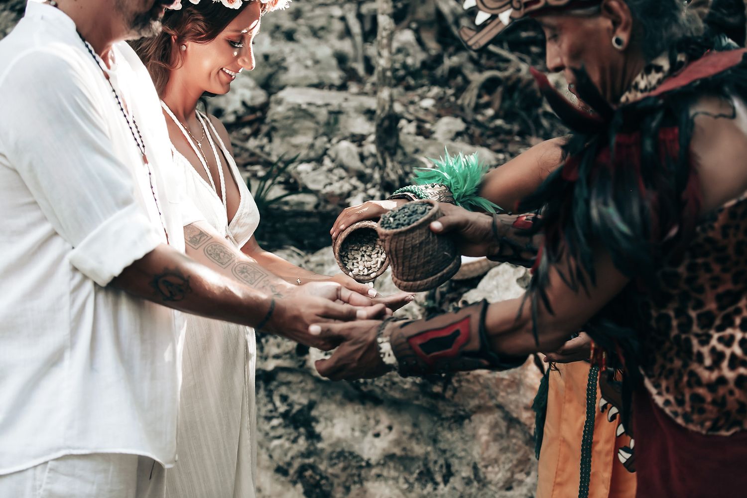 A couple performing a traditional ceremony in a tropical forest, with a person in ceremonial dress.