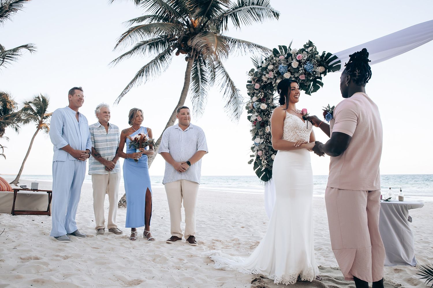 A group of people stand together on a beach, with a bride and groom in the center.