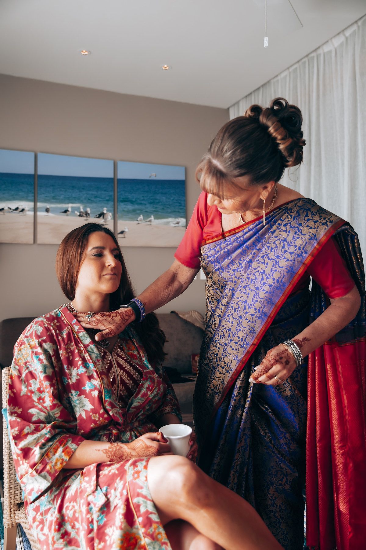 Getting ready scene with women in floral robes helping with traditional Indian wedding preparations.