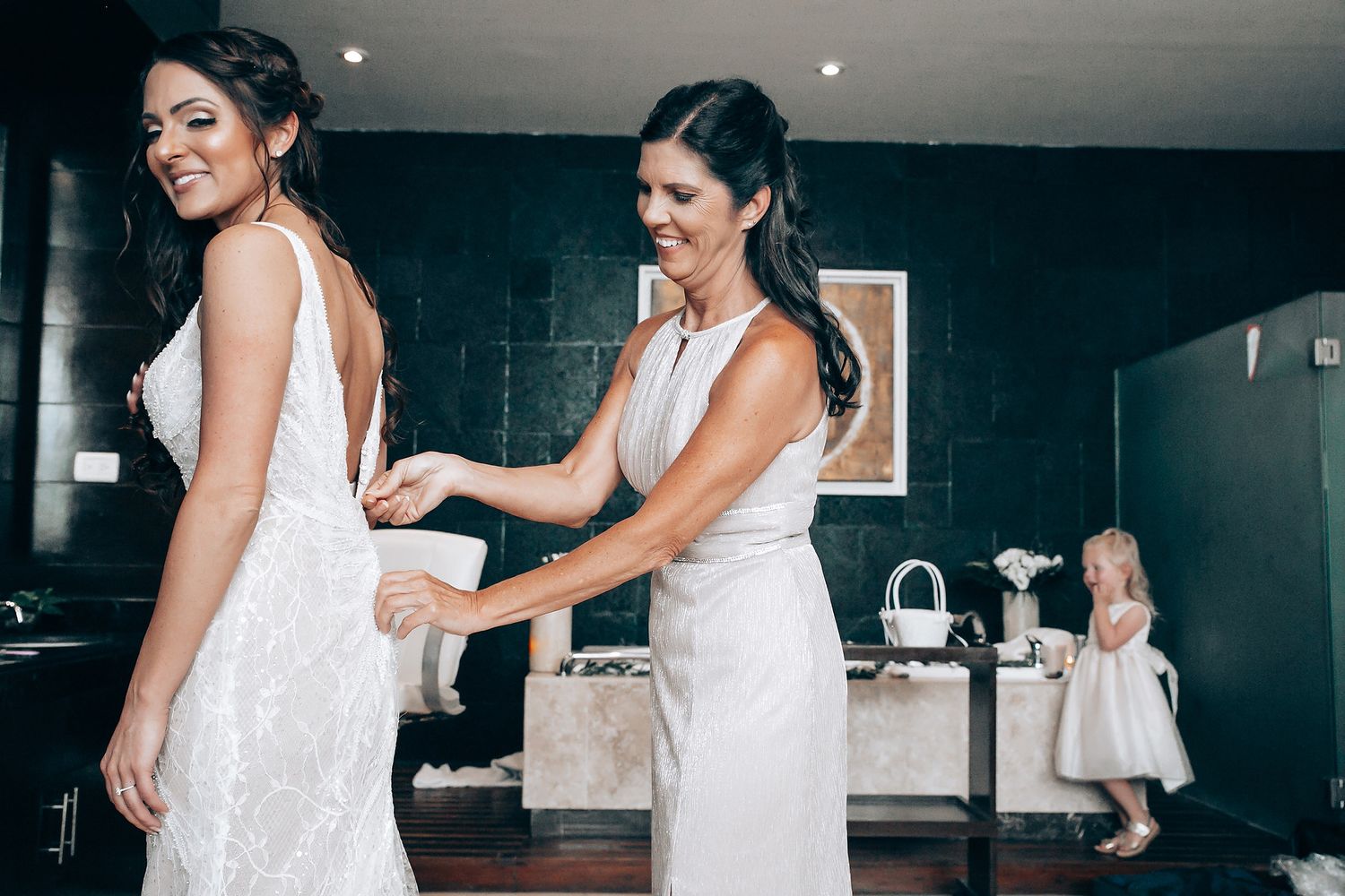 A sequence of getting ready moments shows a white dress being fastened in an elegant indoor setting.