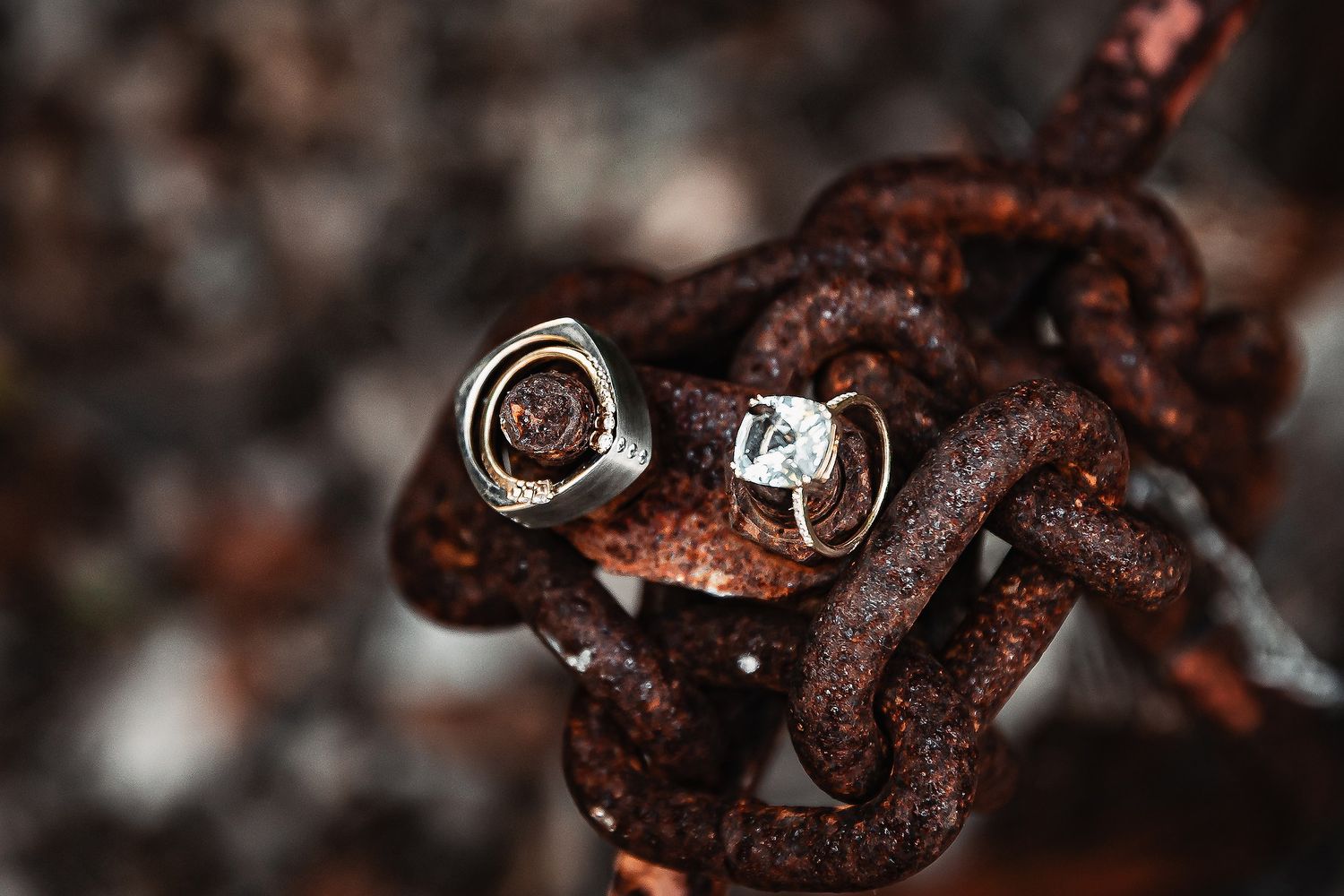Two elegant wedding rings resting on a rusty chain, contrasting delicate diamonds with aged metal texture.