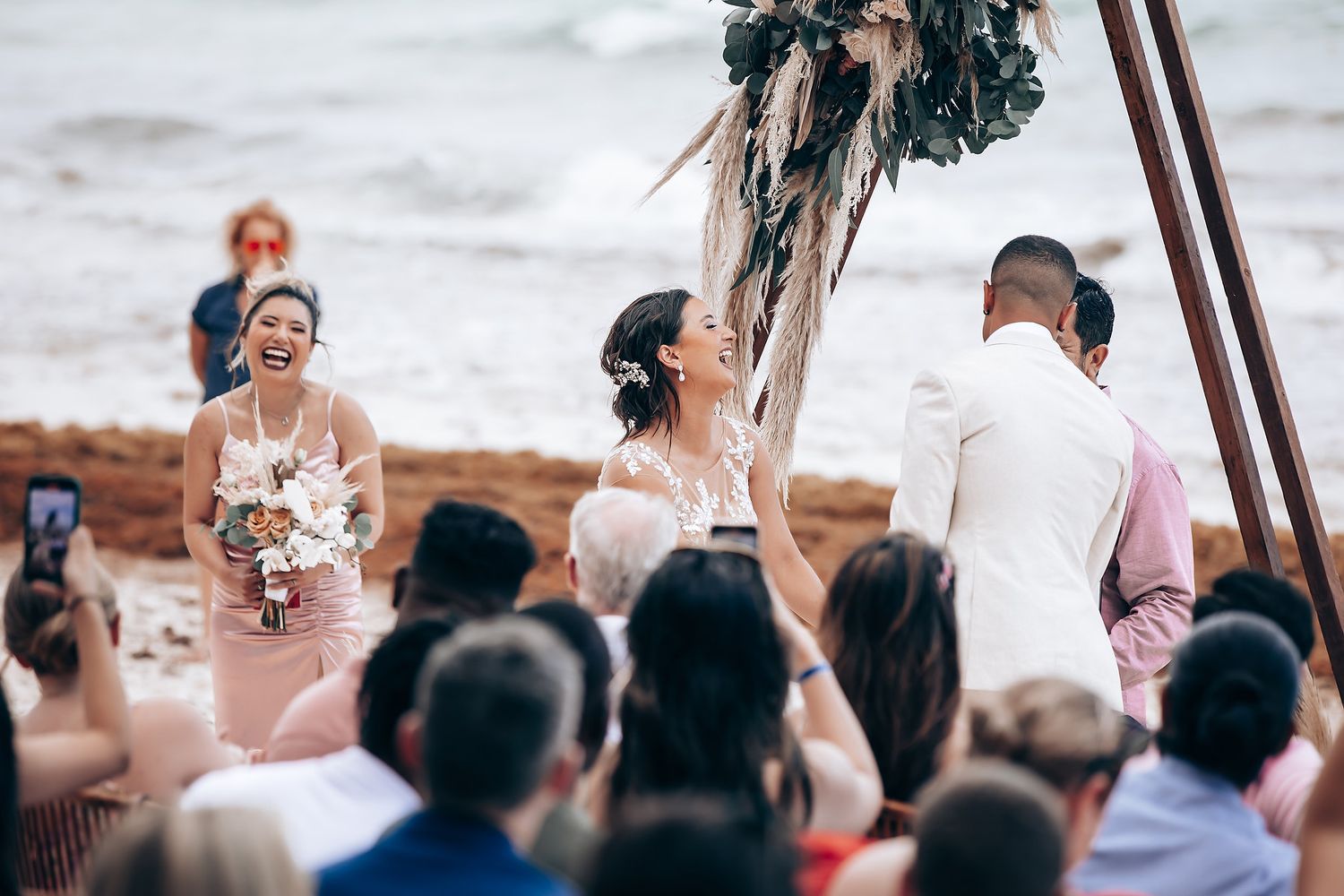 Outdoor wedding ceremony on sandy beach with tropical palm trees and wooden arch.