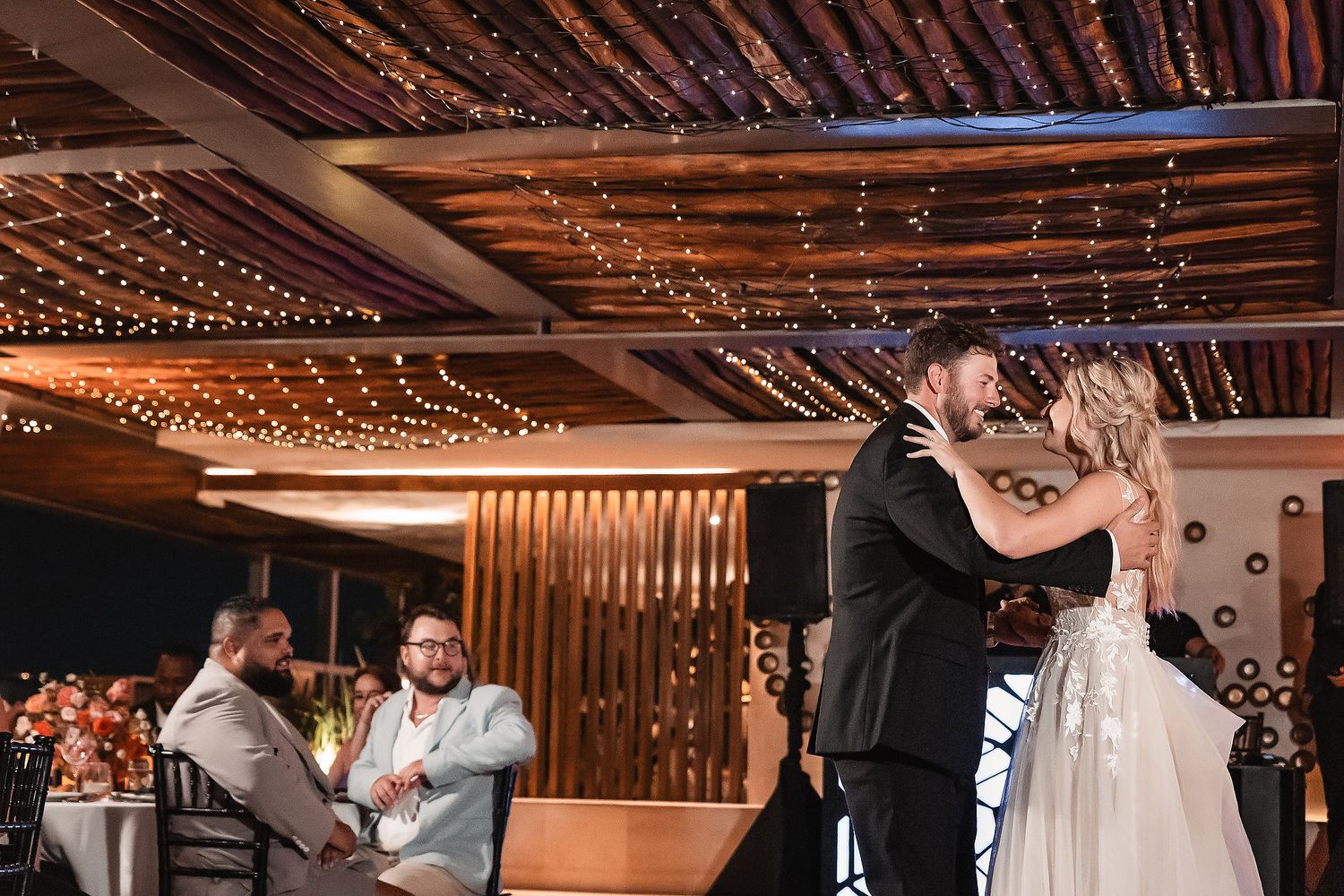 Reception venue decorated with warm string lights and wooden beam ceiling.