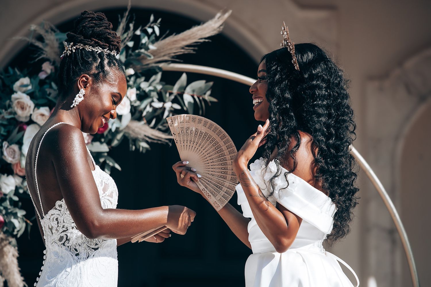 Two women in white dresses sharing a moment with decorative fan.