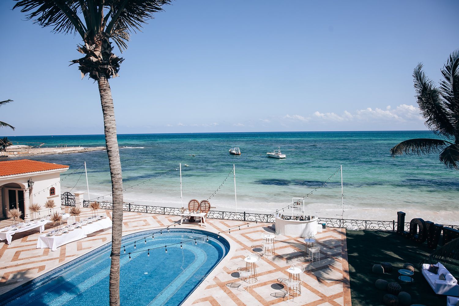 Beachfront resort view with palm trees, swimming pool, and turquoise ocean waters.