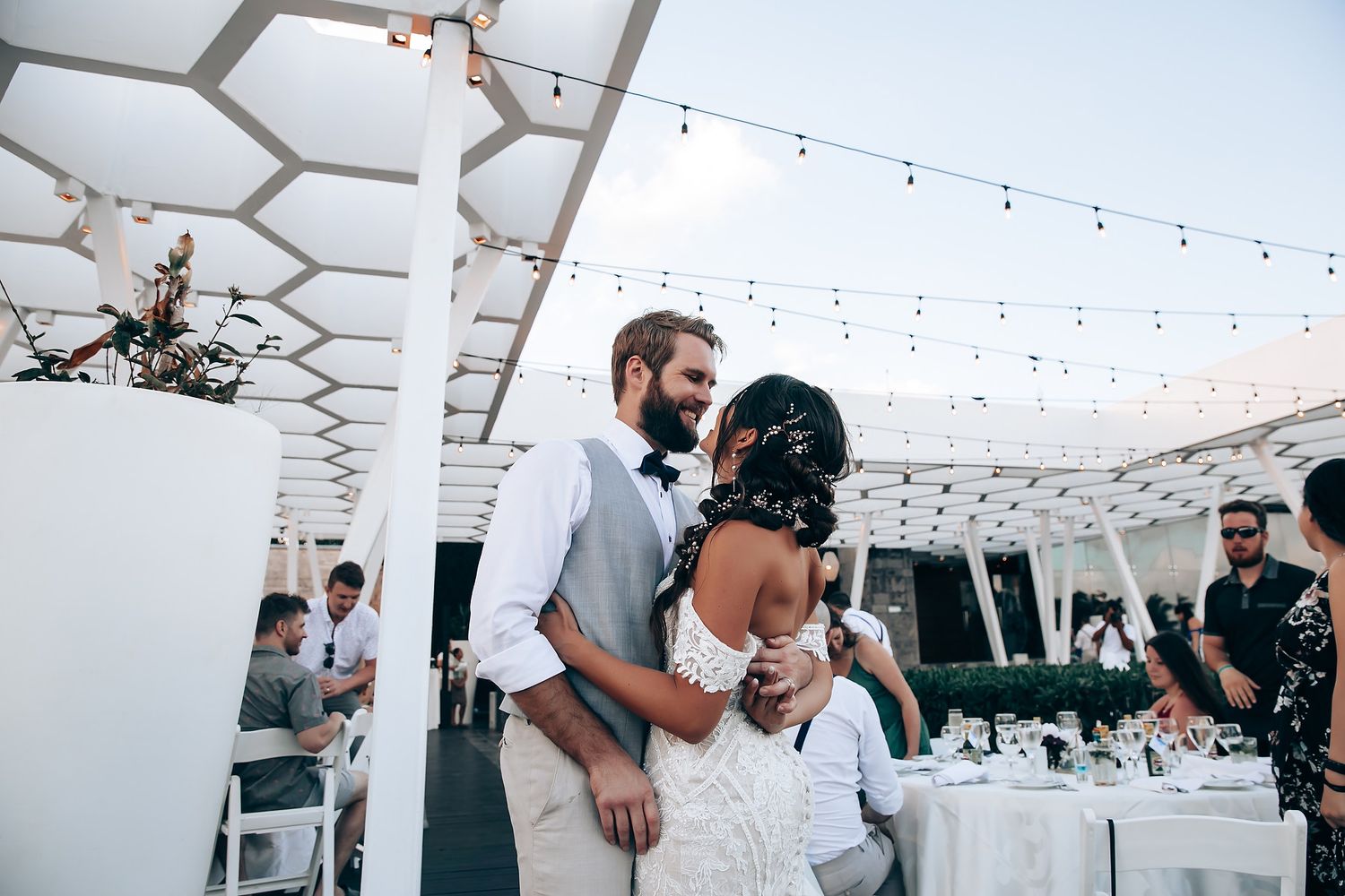Modern white reception venue with geometric ceiling details and hanging string lights.