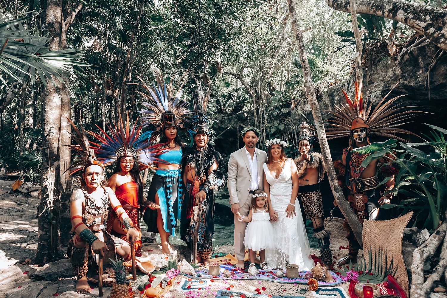 A festive outdoor celebration with guests seated at long tables under tropical foliage.