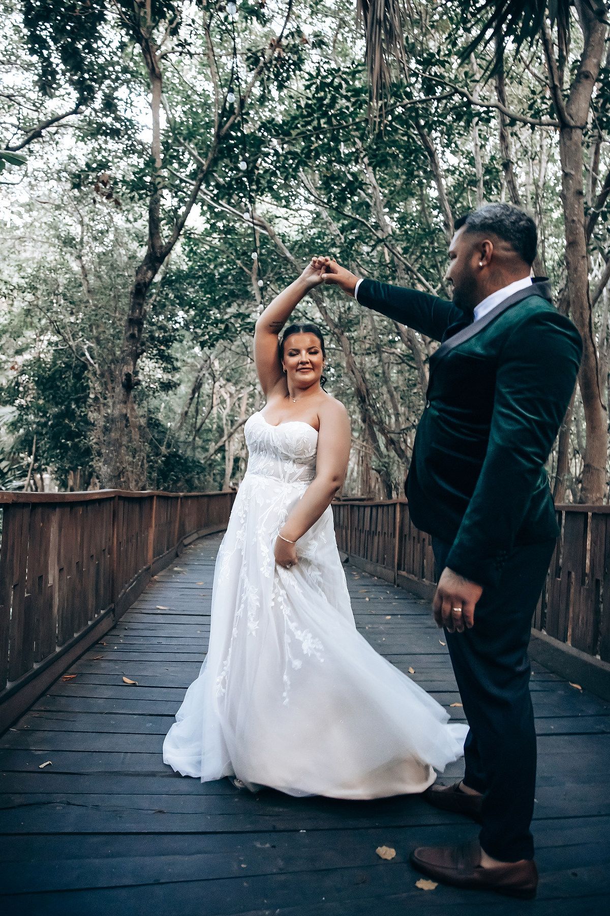 Couple dancing together on a wooden boardwalk surrounded by lush forest scenery.