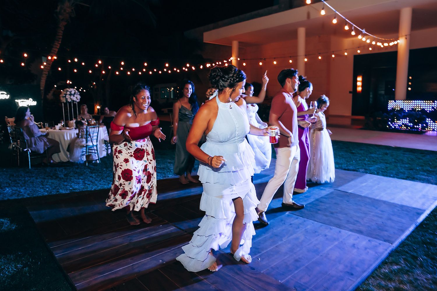Wedding guests dance on an outdoor patio under glowing string lights at dusk.
