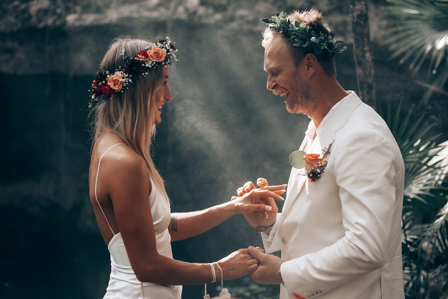 A couple shares an intimate moment during their wedding ceremony wearing floral crowns and white attire.