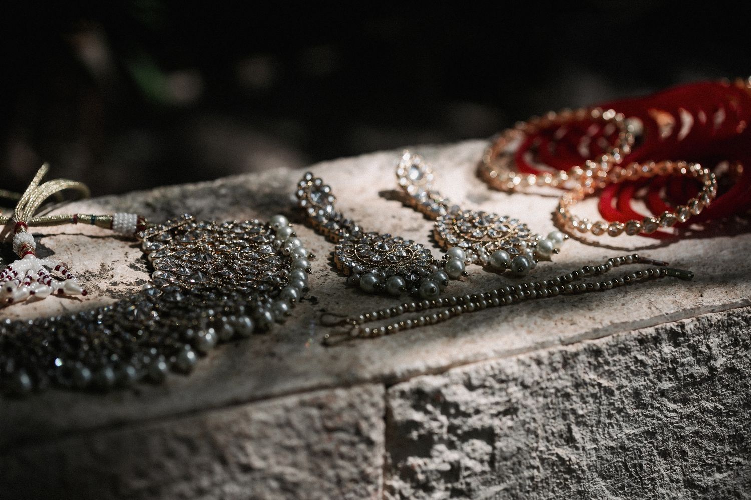 Elegant beaded jewelry including intricate gray earrings and red coral bracelets displayed on a stone surface.