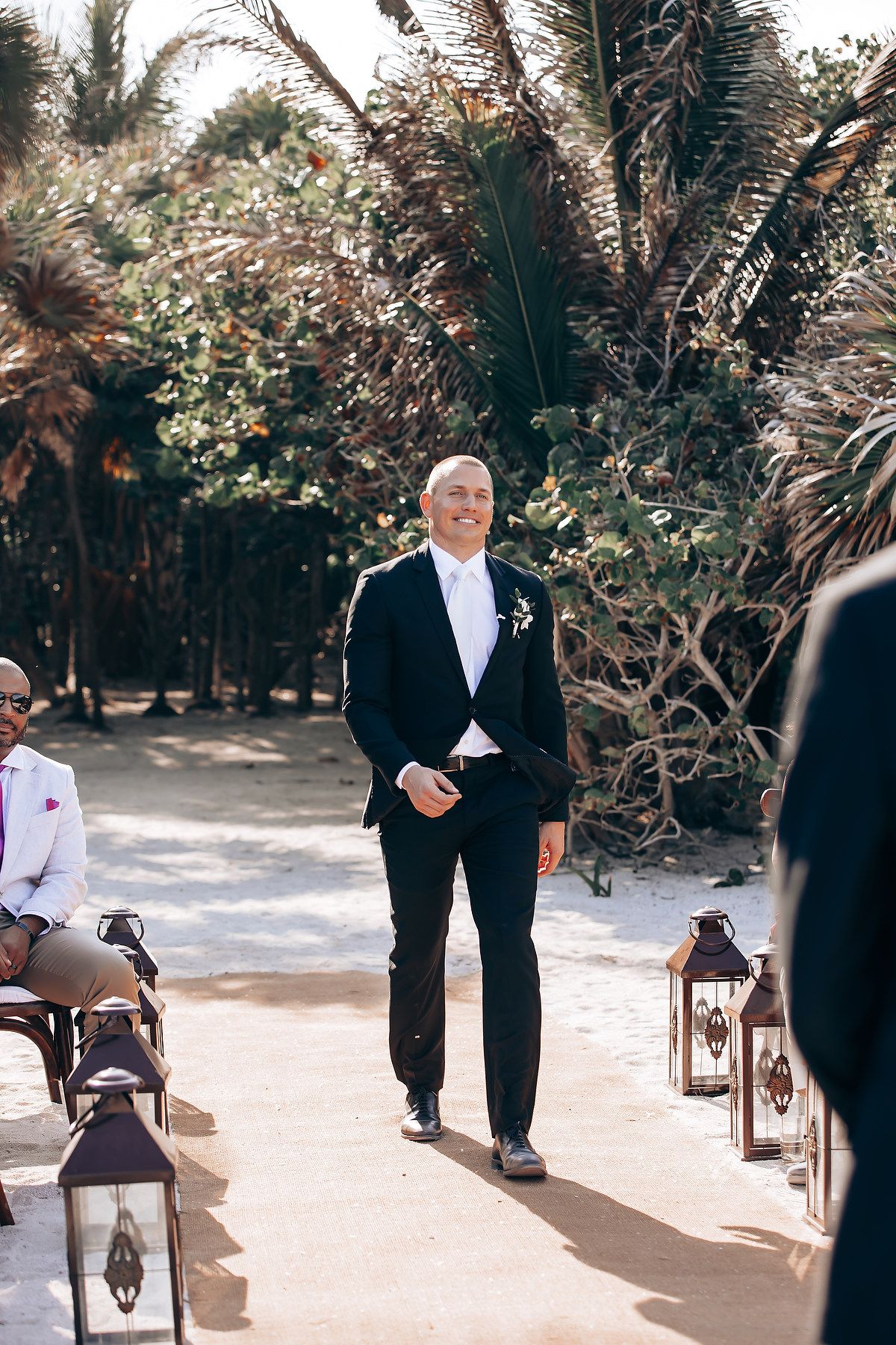 Outdoor wedding ceremony with guests seated on white chairs along a garden path.