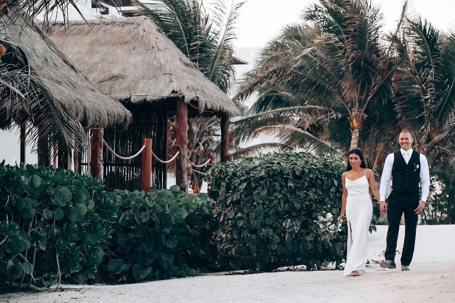 A series of wedding photos capturing newlyweds walking and posing together on a tropical beach path with palm trees.