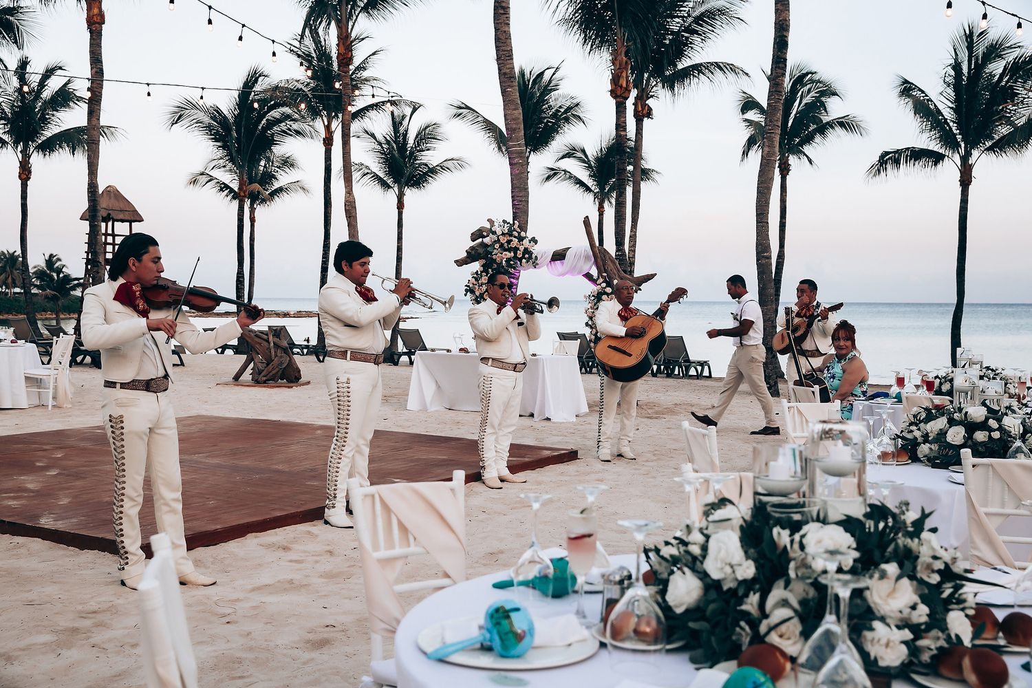 Musicians in white uniforms perform at a beachside wedding reception with string instruments and guitar.