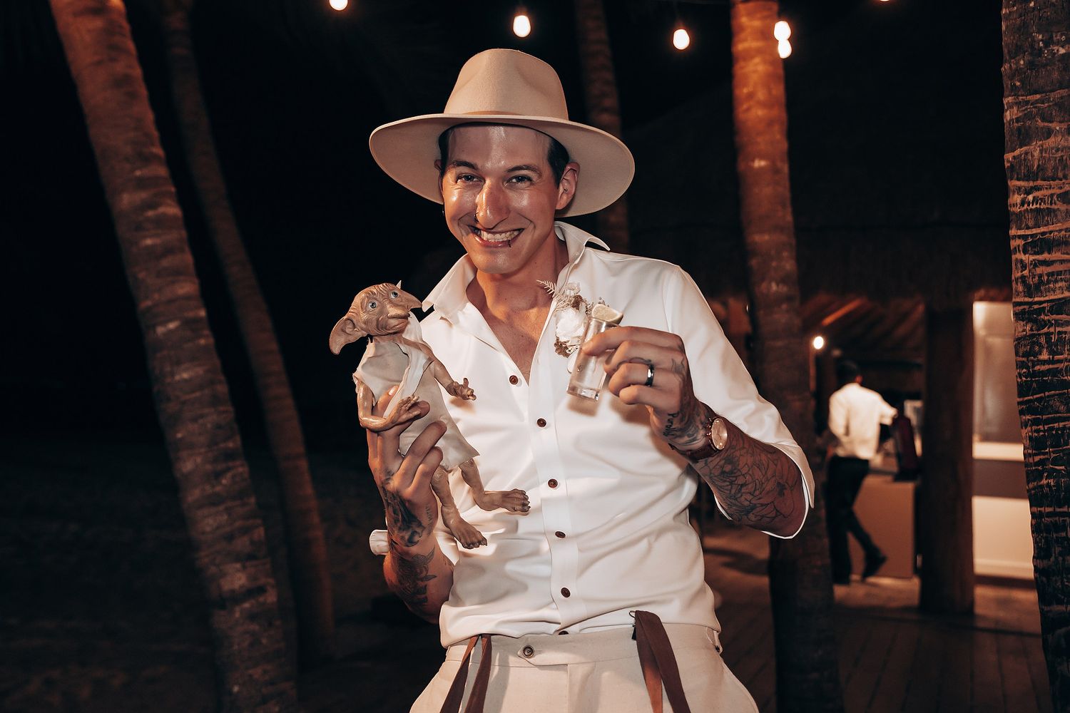 Nighttime celebration under string lights with tropical palm trees in background.