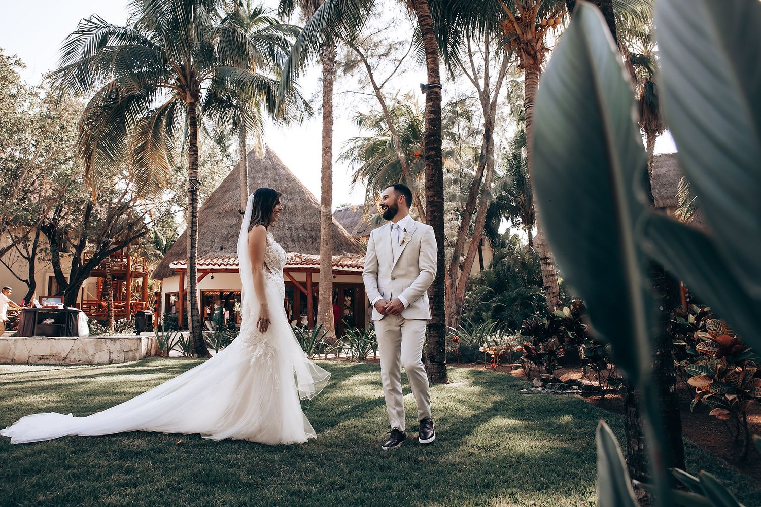 Wedding ceremony setup with palm trees and thatched-roof buildings in background.