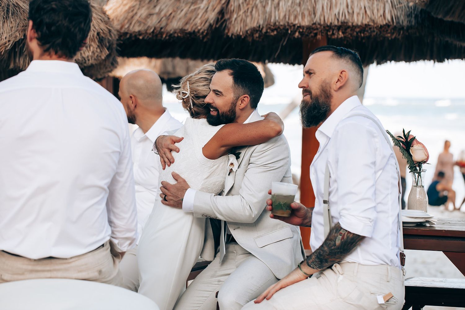 Group of wedding guests in white attire celebrating joyfully at an outdoor reception.