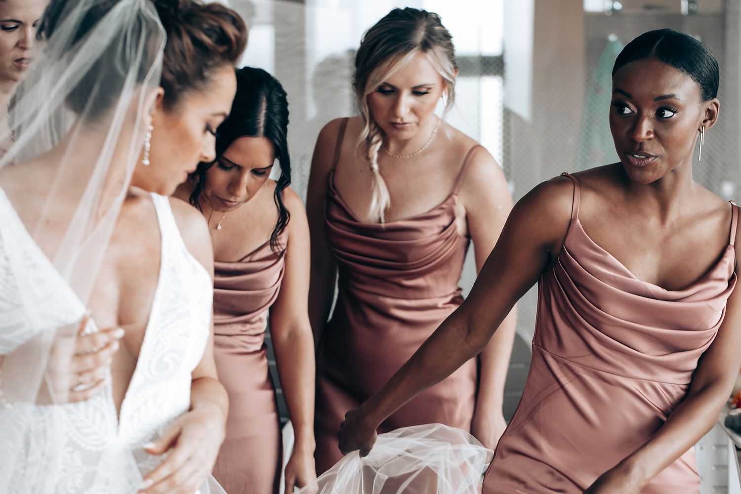Wedding party wearing dusty rose bridesmaid dresses stand together in elegant poses.