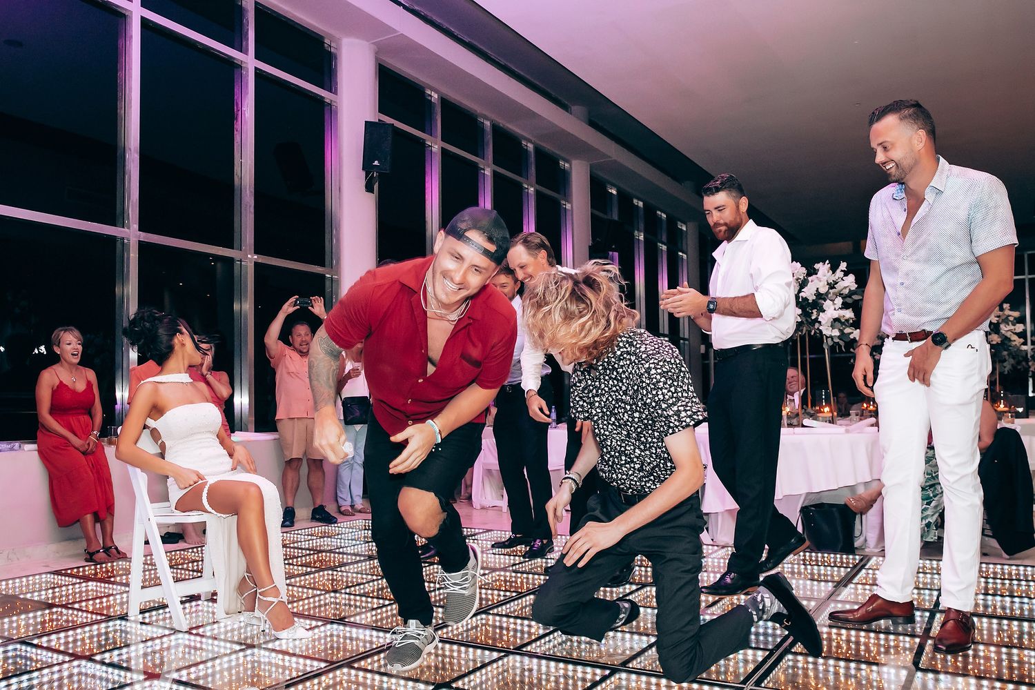 Wedding guests enjoying reception activities under pink ambient lighting.