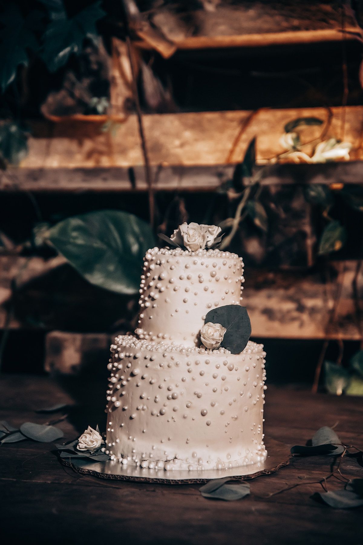 A classic white wedding cake with delicate pearl decorations displayed in moody lighting.